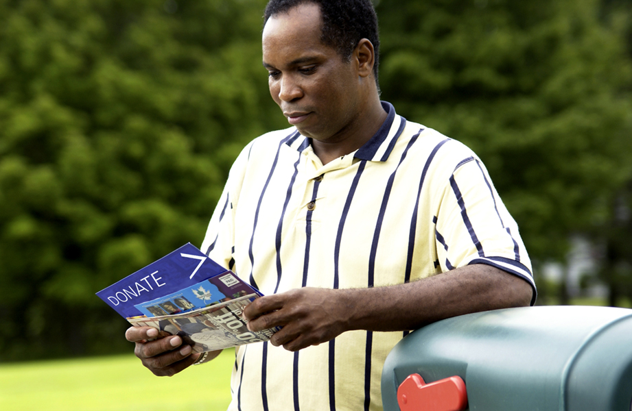 Man next to a mailbox holding nonprofit direct mail flyers