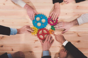 multiple people's hand holding gears in the middle of a conference room table